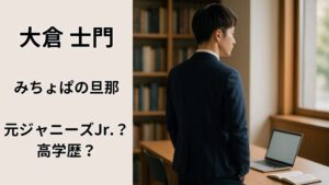 静かな大学図書館で本棚とノートPCの前に立つスーツ姿の日本人男性の後ろ姿。みちょぱの旦那・大倉士門の知的なイメージを表現した写真。
