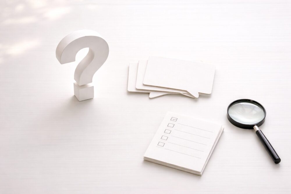 大きな無地の疑問符と虫眼鏡で「FAQ」を表現したデスク俯瞰イメージ