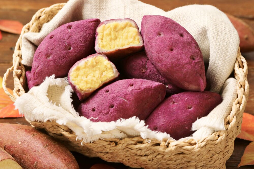 ハートブレッドアンティークで販売されている、本物のサツマイモそっくりのコグマパン（さつまいもパン）。カゴに盛られたパンの断面から、黄金色の餡がたっぷり詰まっている様子が分かる画像。