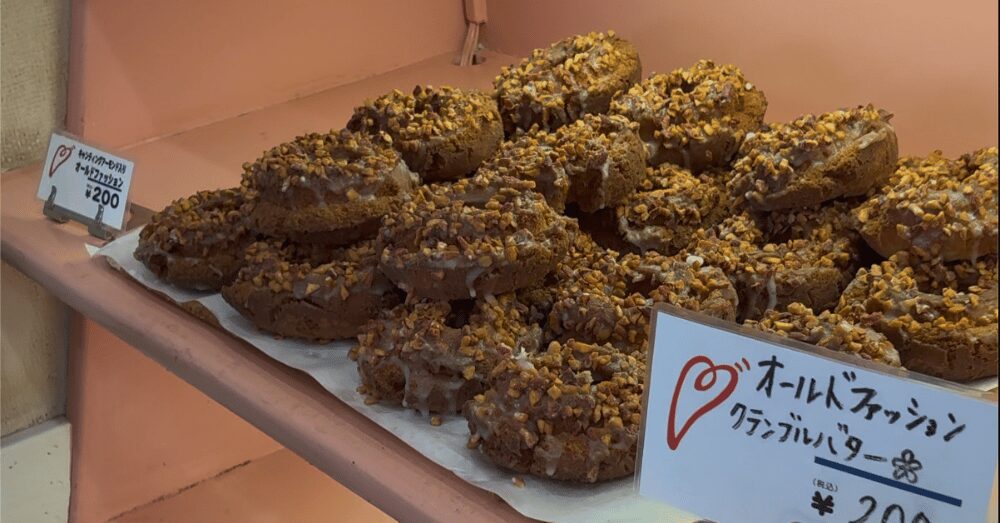 ハッピードーナッツのおすすめメニュー「オールドファッション クランブルバター（税込200円）」。たっぷりのナッツとクランブルがトッピングされた、ザクザク食感が魅力のドーナツ。