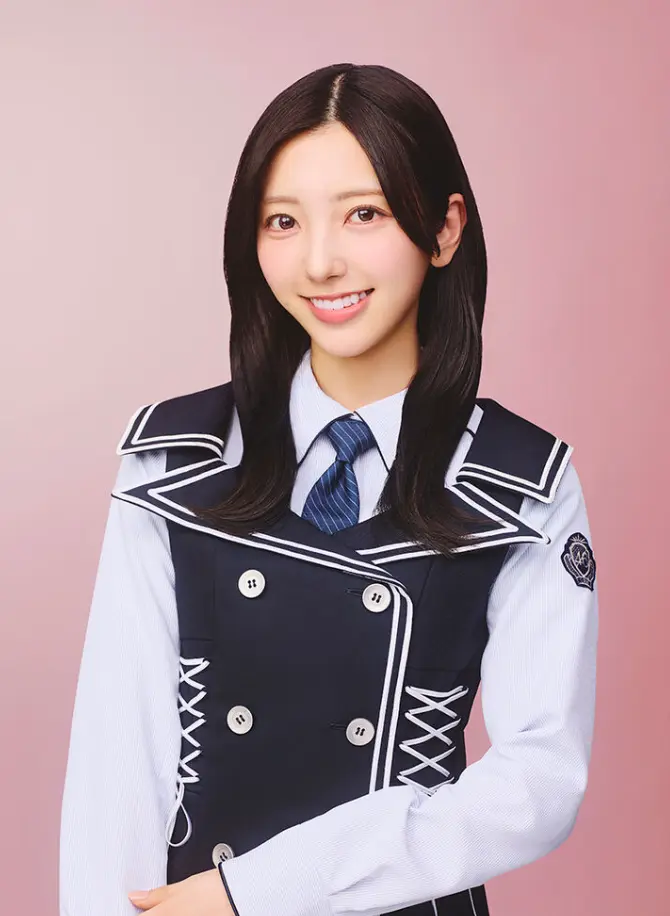 日向坂46のメンバー、小西夏菜実さんの公式プロフィール写真。ピンクの背景に、ネイビーブルーとホワイトの制服姿で、優しく微笑んでいる上半身のショット。