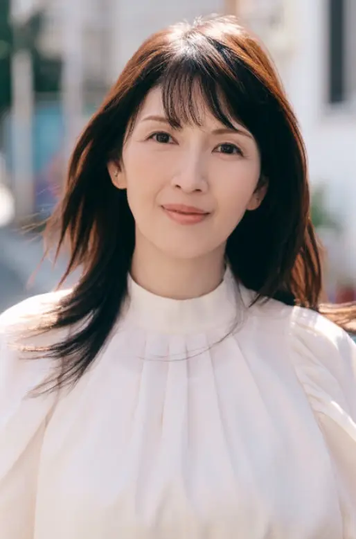 白いブラウスを着て、優しく微笑む女優・吉井怜さんのプロフィール写真。背景は柔らかな街並みのボケ。
